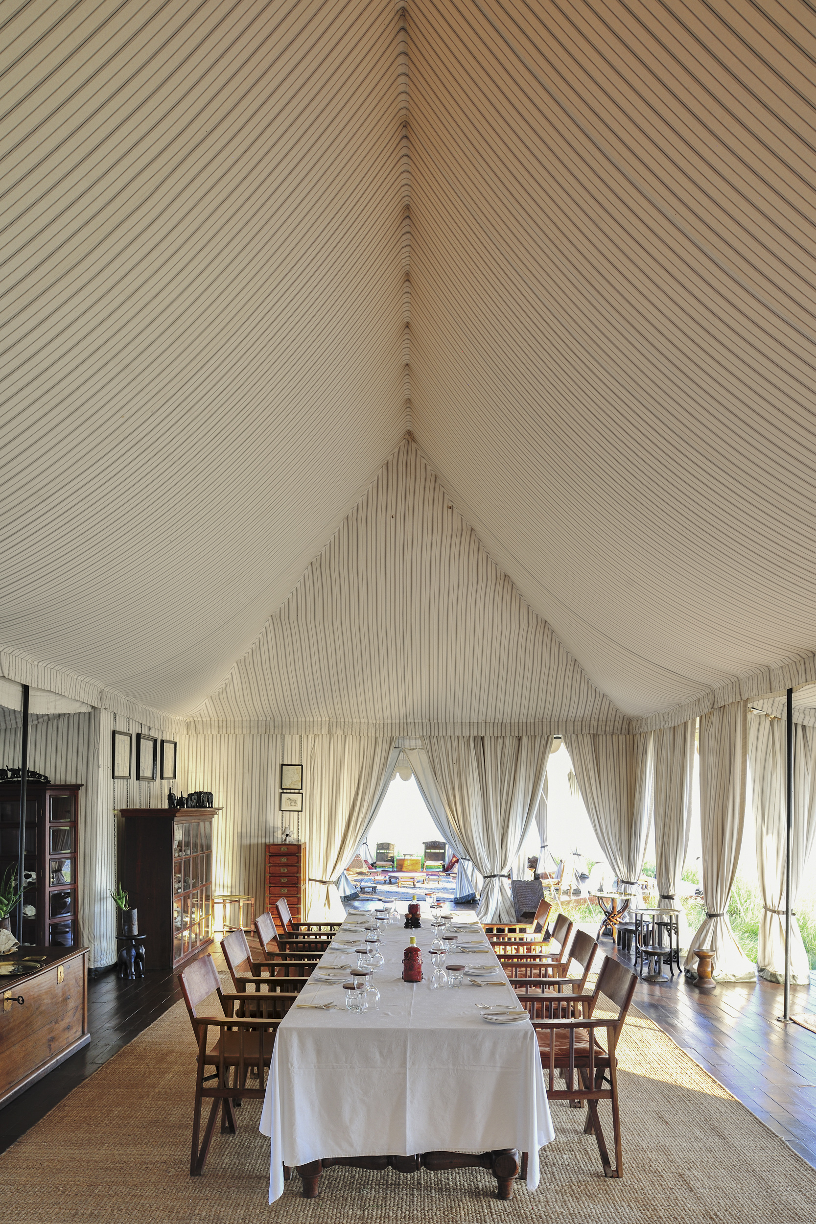 A grand tented dining area adorned with wooden furniture and crisp white table settings.