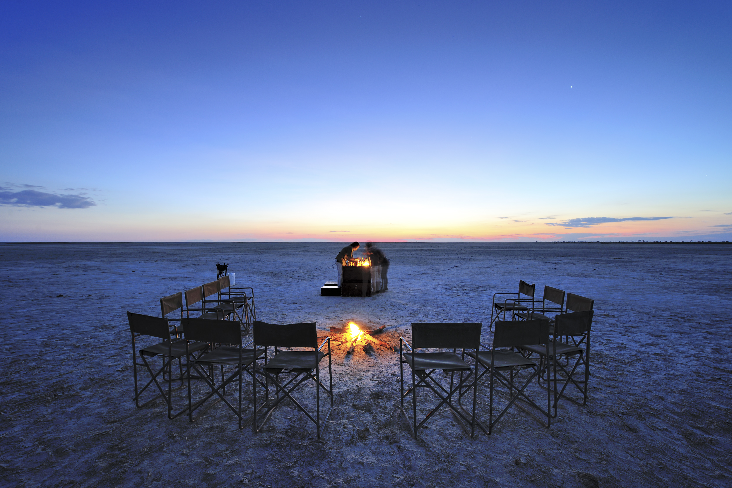A magical evening setup with chairs encircling a campfire under a brilliant dusk sky.