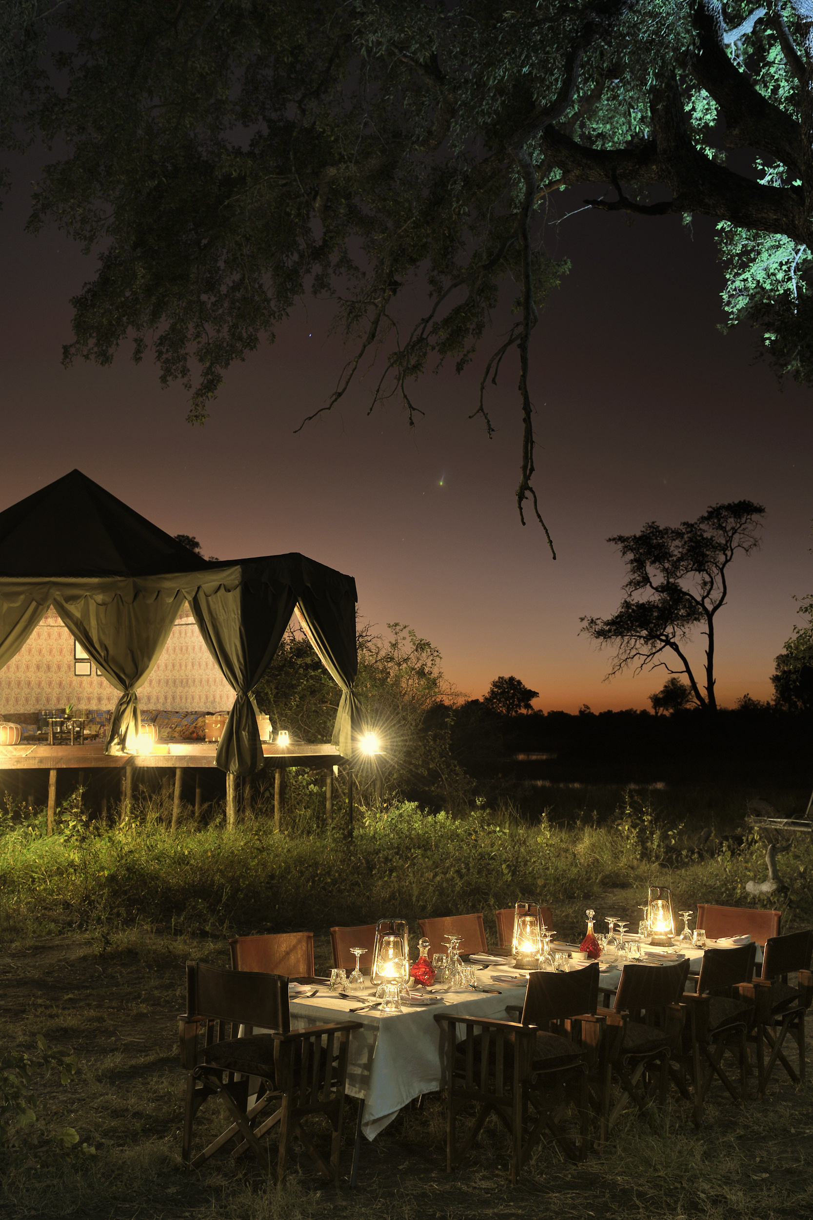 Lantern-lit dining at Duke's Camp, with a glowing tent and dusk sky in the wilderness.